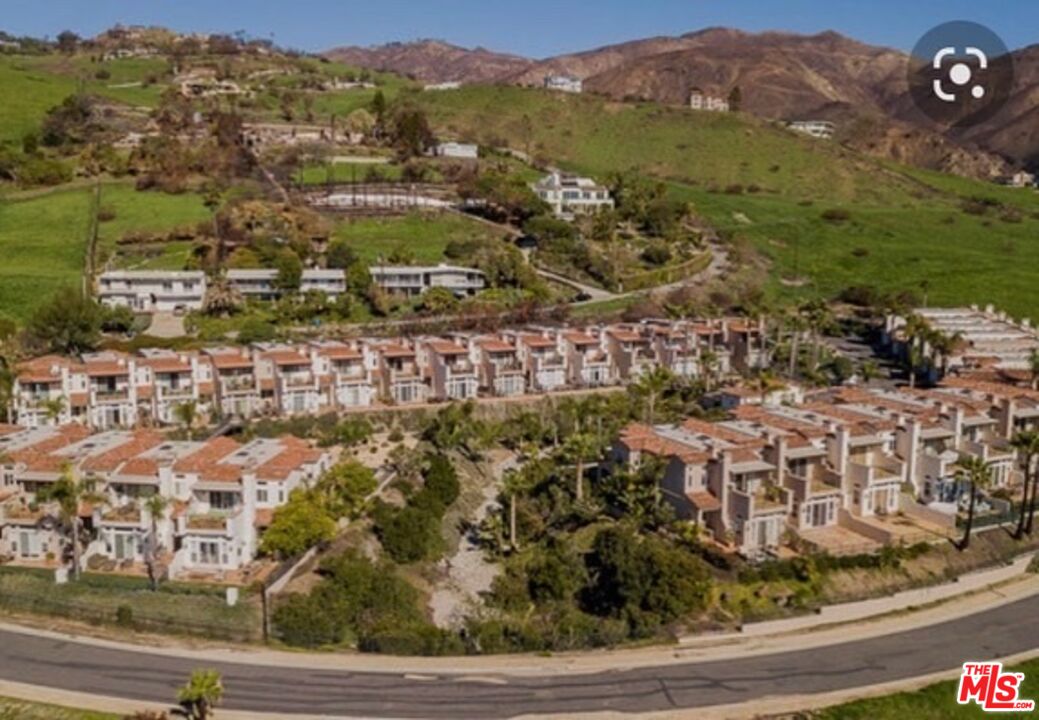 Aerial view of rows of homes beside a curved road, with rolling hills in the background.