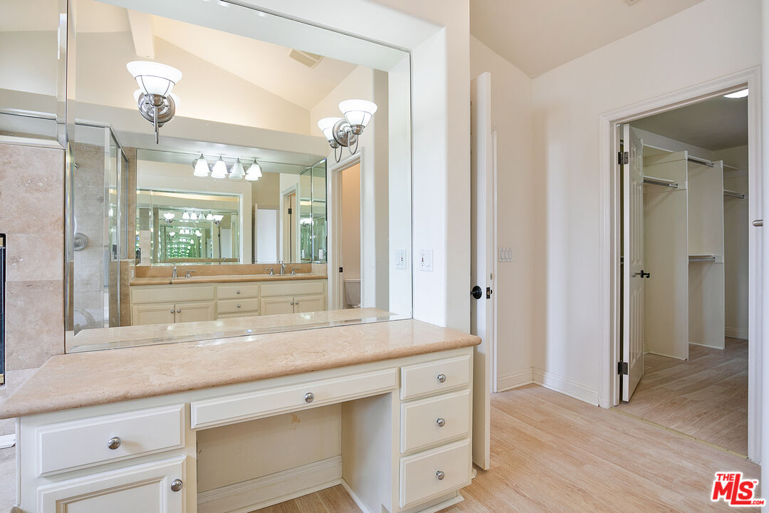 Bathroom with a long cream vanity, large mirror, and doorway to a walk-in closet.