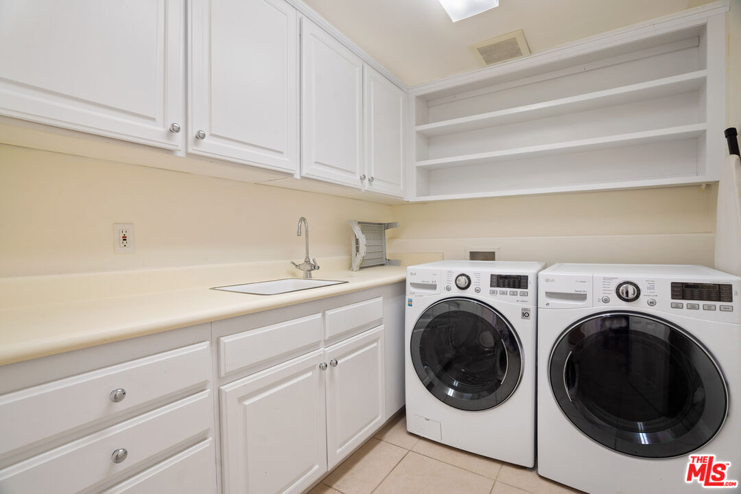 Laundry room with front-loading washer and dryer beside a utility sink and white cabinets.