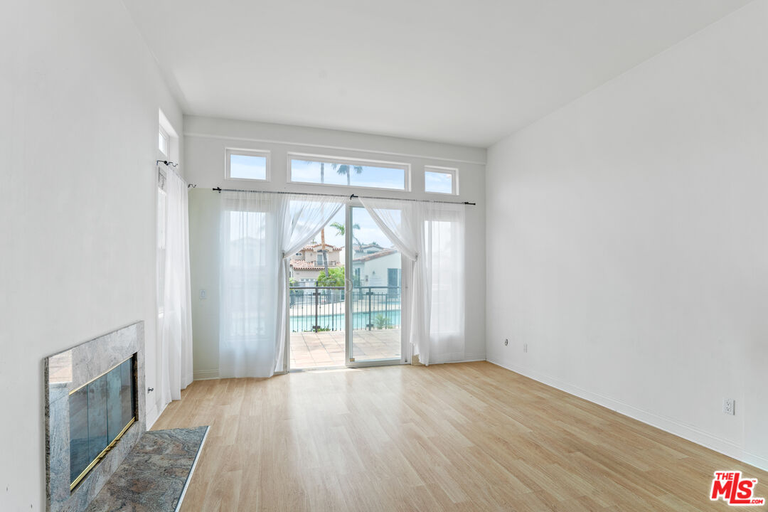Empty living room with a stone fireplace and sliding doors opening to a patio and pool.