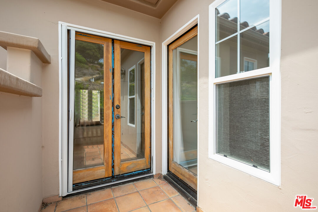 Home entry patio with terracotta tile and wood-framed glass double doors beside a large window.