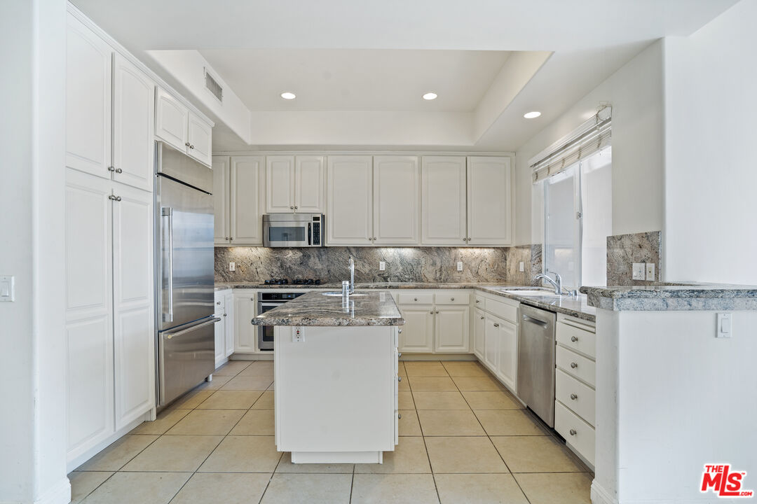 Kitchen with white cabinets, a granite island, stainless steel appliances, and tiled floors.