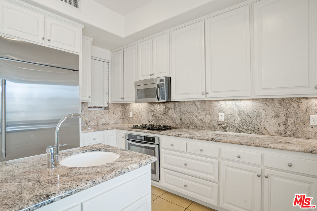 Kitchen with white cabinetry, granite counters, stainless steel appliances, and a peninsula sink.