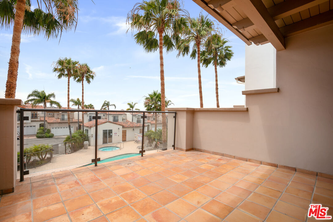 Empty tiled balcony overlooking palm trees, neighboring homes, and a swimming pool.