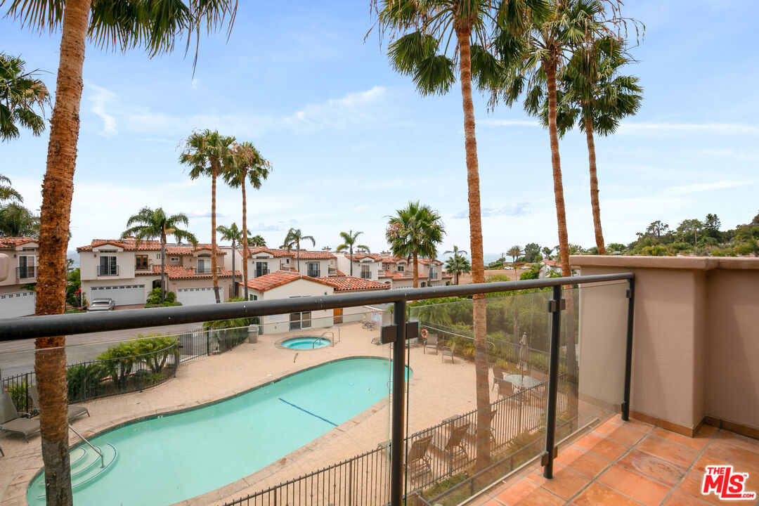 Balcony overlooking a turquoise pool, neighboring homes, and tall palm trees.