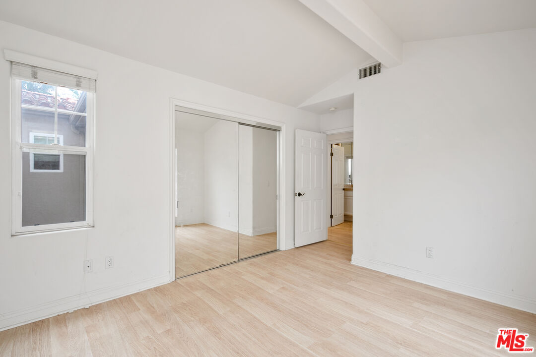 Vacant bedroom with mirrored closet doors, pale wood flooring, and a window.