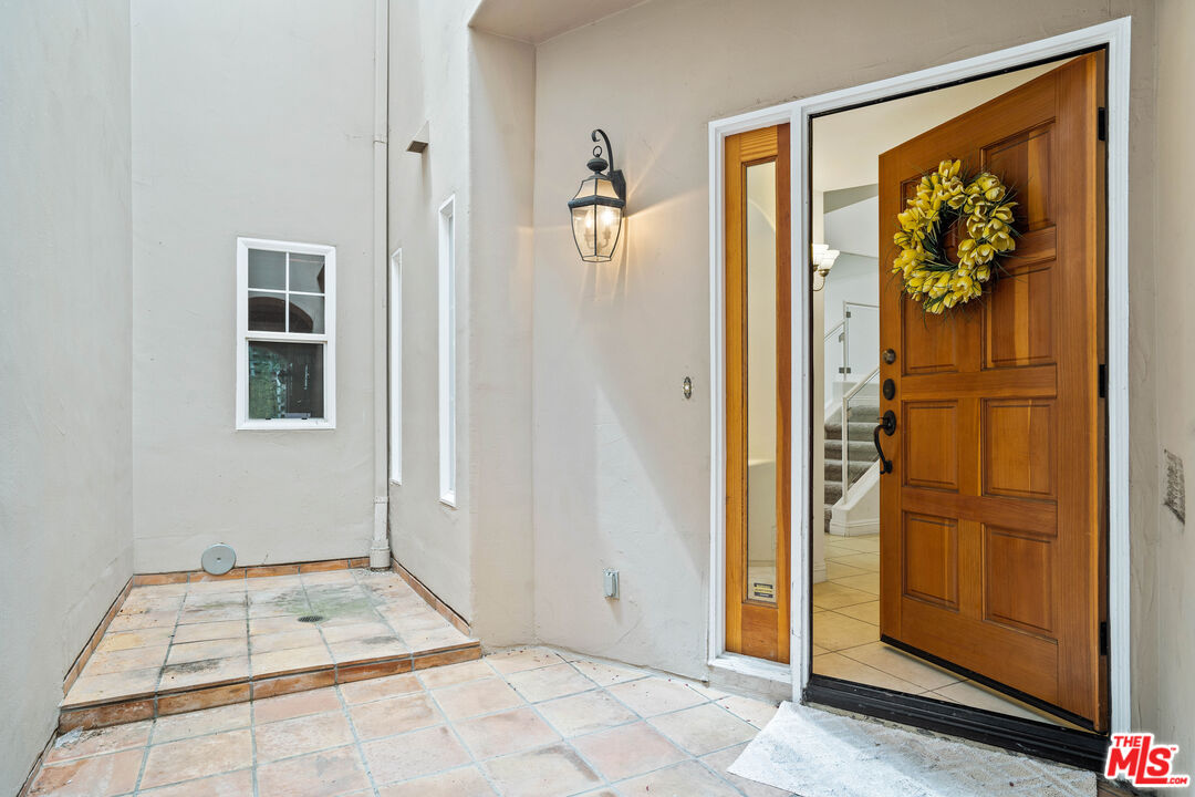 Front entry with an open wooden door, yellow wreath, tiled porch, and wall lantern.