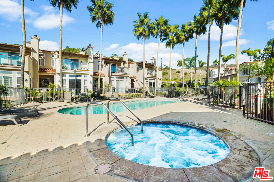Residential complex pool and bubbling spa framed by palm trees and homes with balconies.