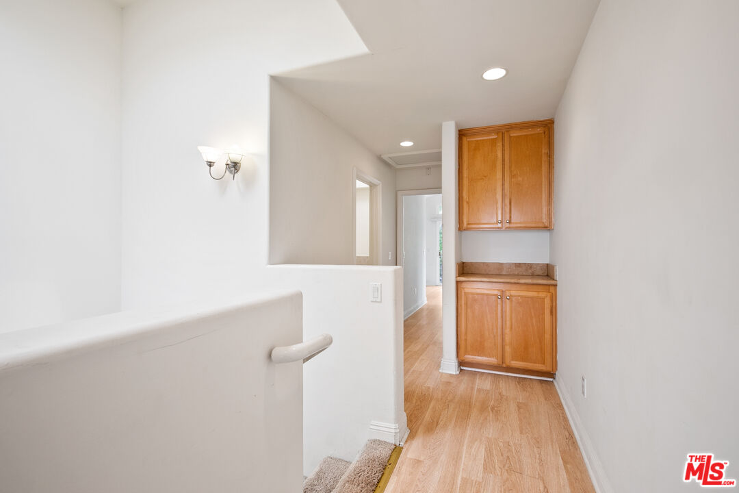 Hallway with light wood floors, white walls, and built-in honey-colored cabinets.