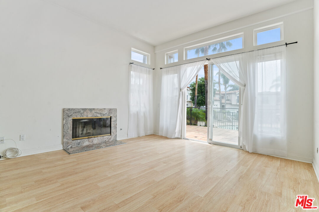 Empty living room with pale wood floors, a stone fireplace, and sliding glass doors opening to a patio.