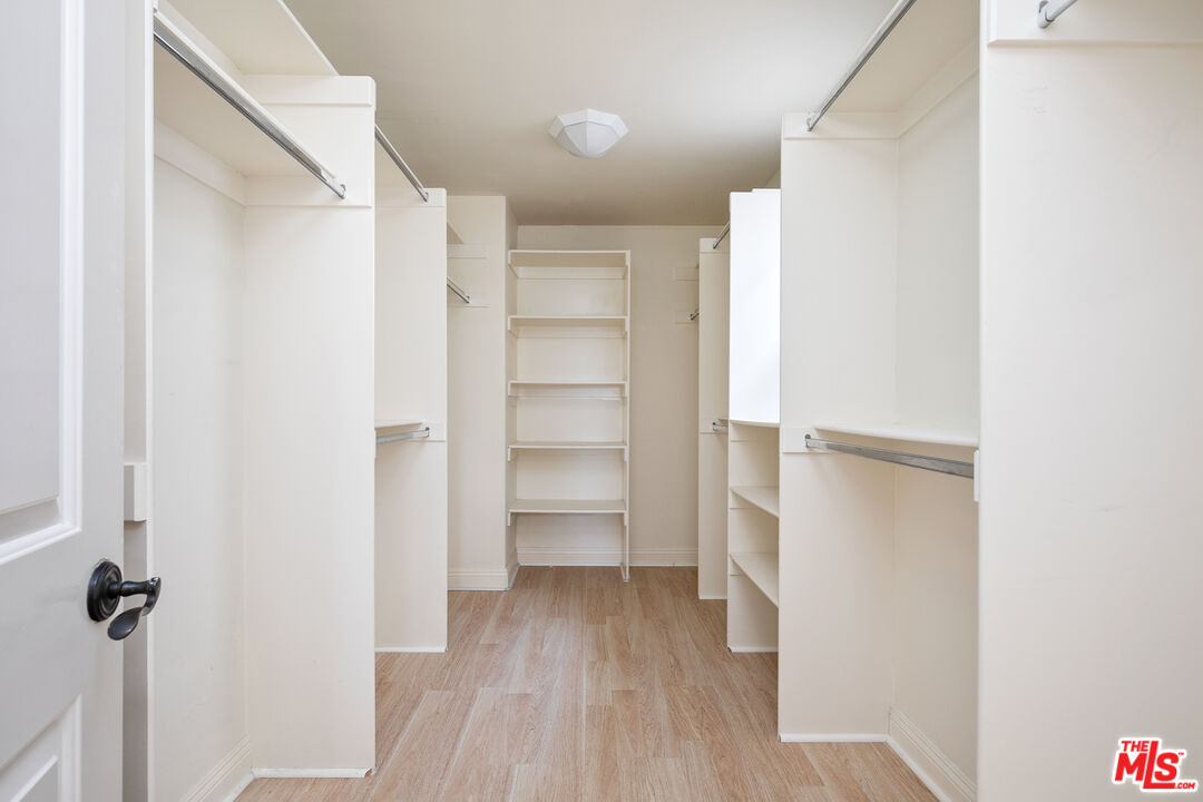 Walk-in closet with built-in shelving, hanging rails, and light wood flooring.