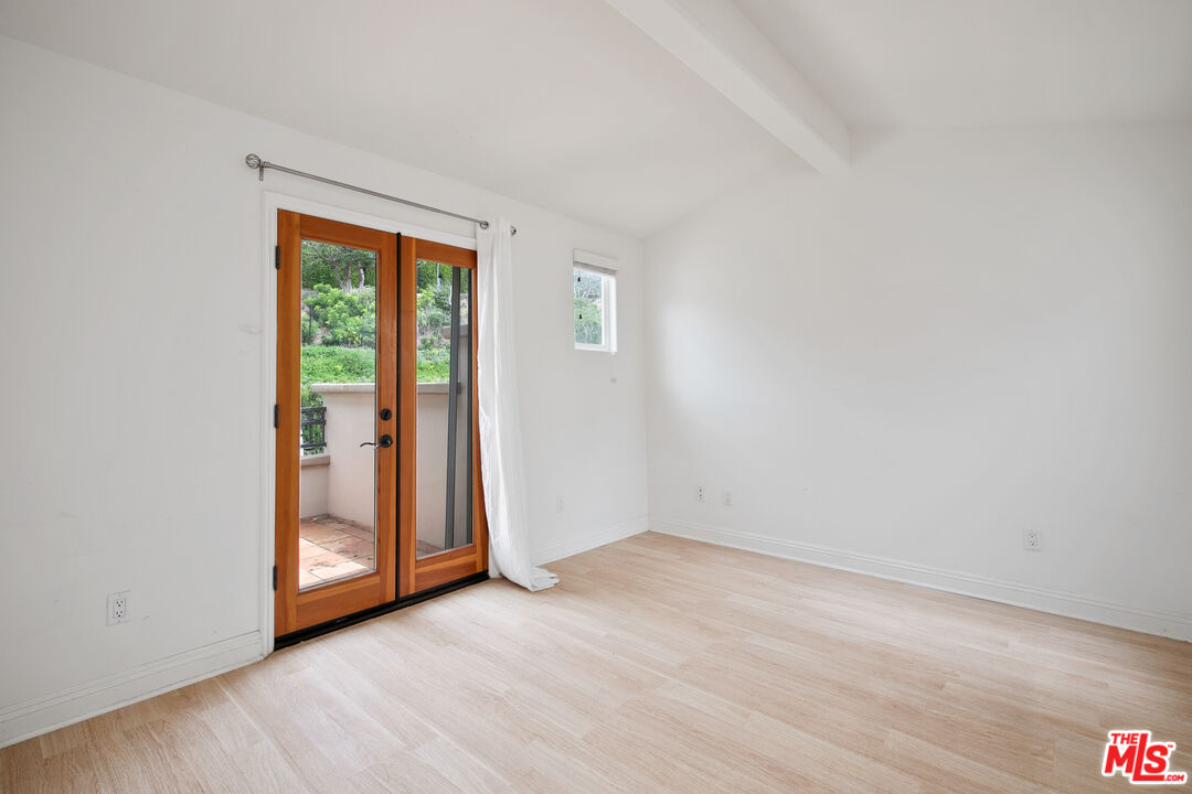 Vacant room with pale wood flooring and wood-framed French doors opening to a patio.