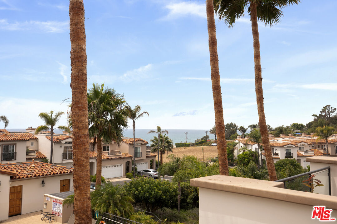 Ocean view over neighboring homes and palm trees from a balcony.