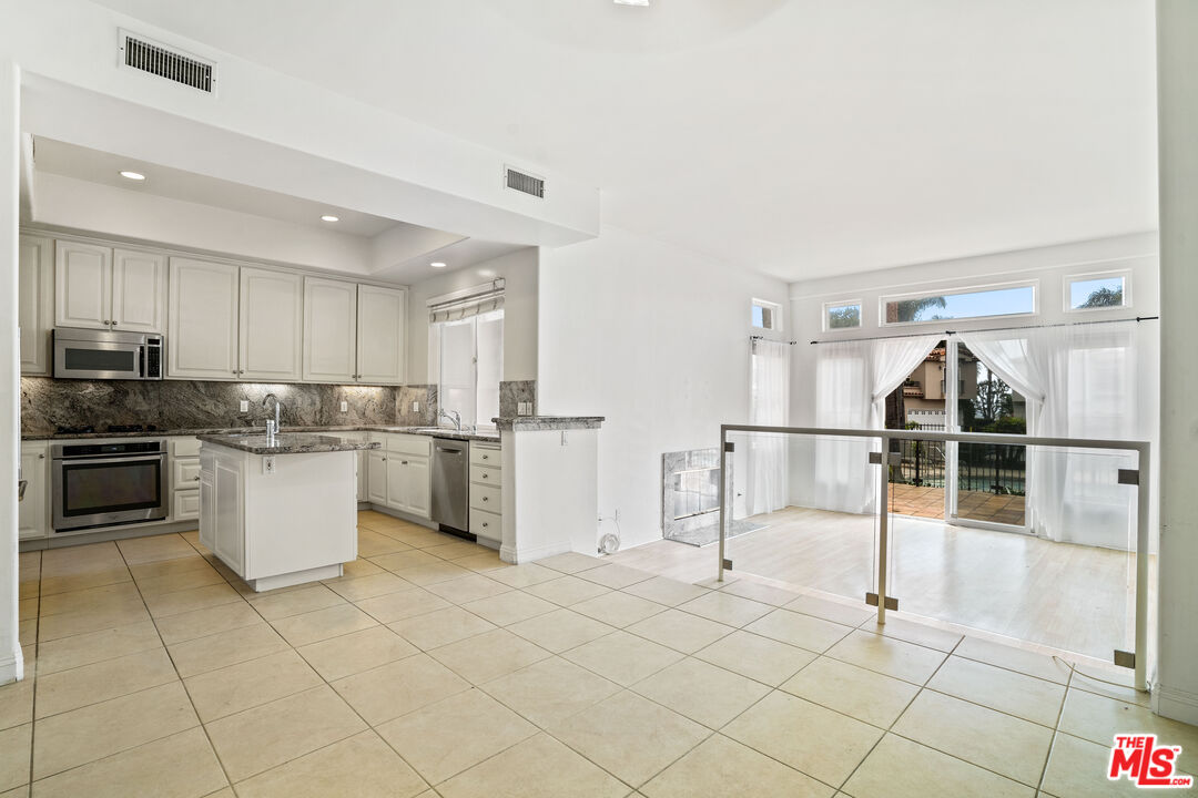 Open-plan kitchen with granite counters and white cabinets beside a glass-railed living area opening to a patio.