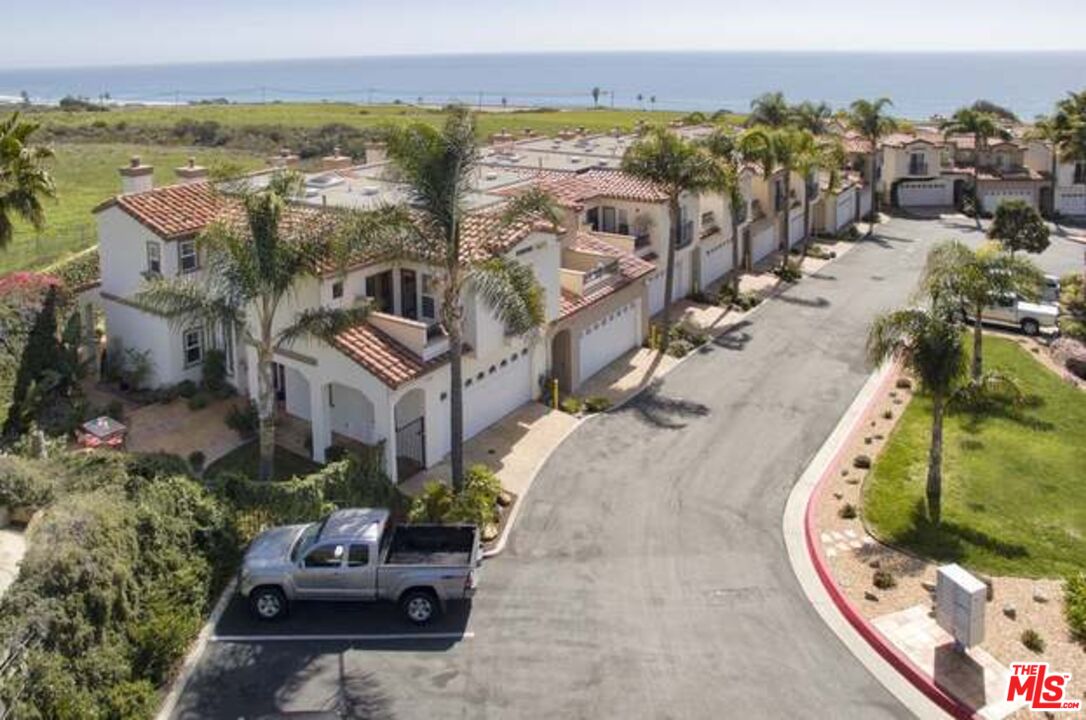 Aerial view of Spanish-style homes beside a curved street, with palm trees and ocean beyond.