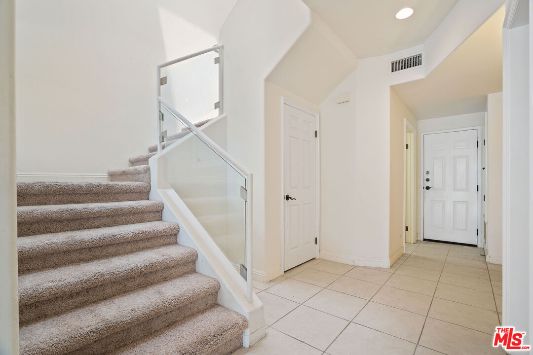 Home entryway with tiled floors and a carpeted staircase behind a glass railing.
