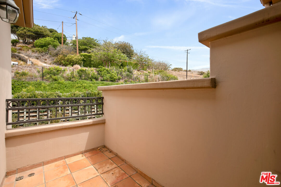 Tiled stucco balcony overlooking a green hillside, framed by a decorative metal railing.