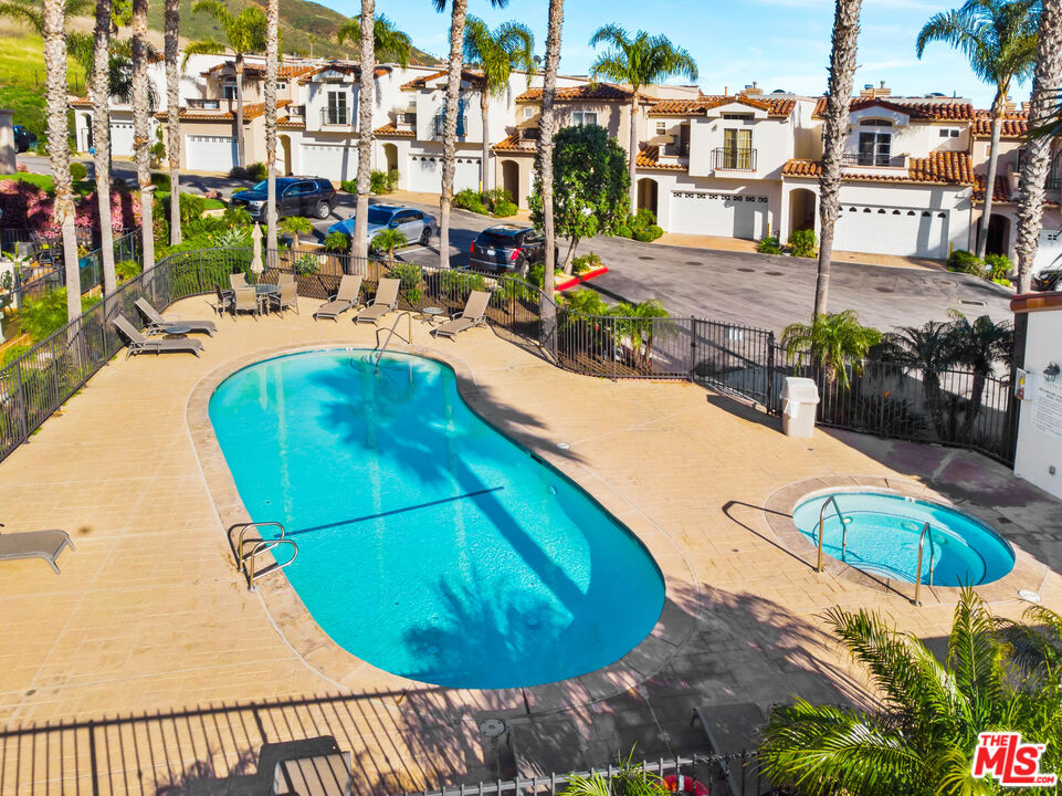 Community pool and spa with lounge chairs, palm trees, and Mediterranean-style homes.