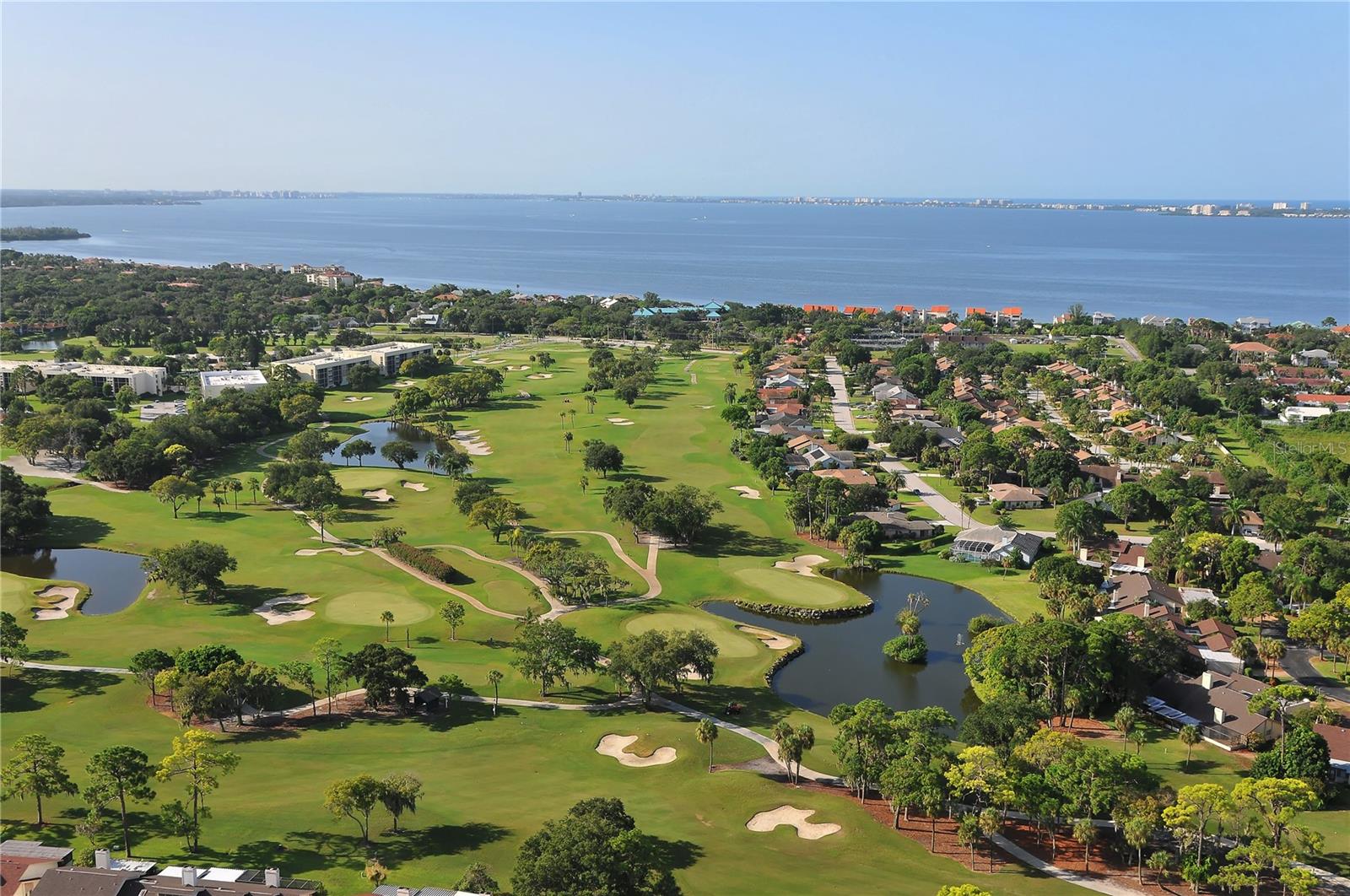 Aerial view of a golf course beside a bay, with homes and landscaped fairways.