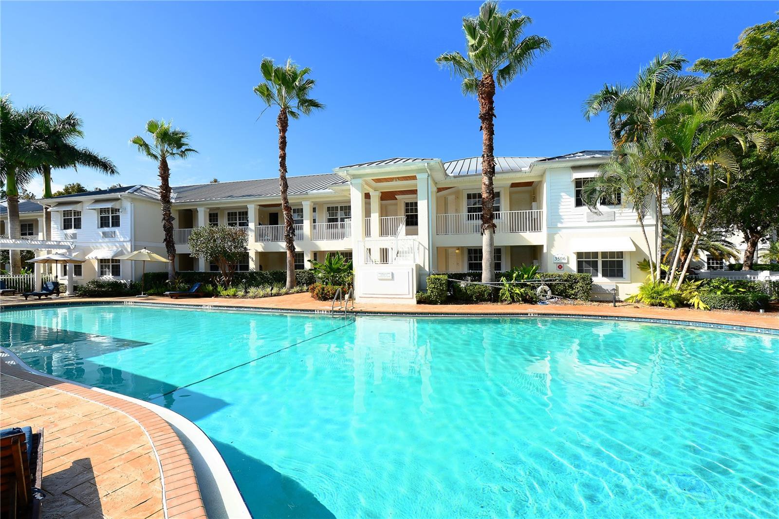 Residential community pool in front of a white two-story building with balconies and palm trees.