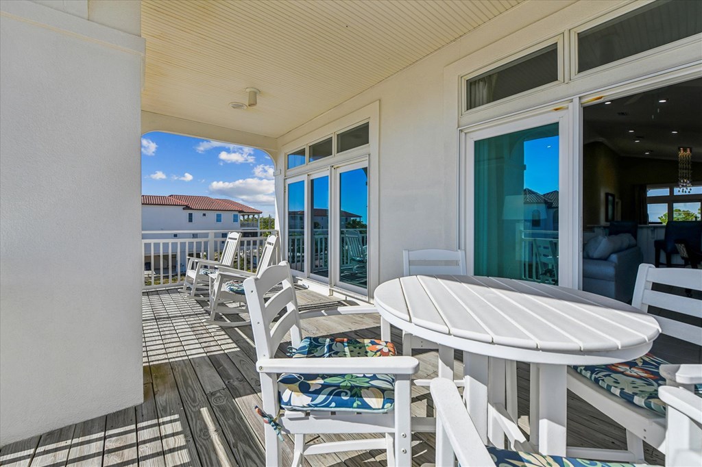 Covered wooden deck with white patio furniture and sliding glass doors.