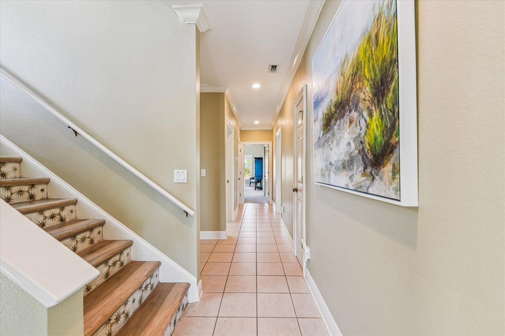 Tiled hallway beside a wooden staircase, with patterned carpet and a large coastal painting.
