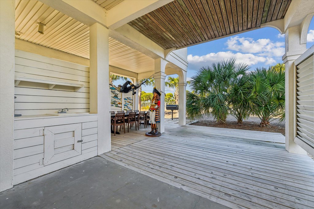 Covered deck with an outdoor grill, dining table, and pirate statue beside palm trees.