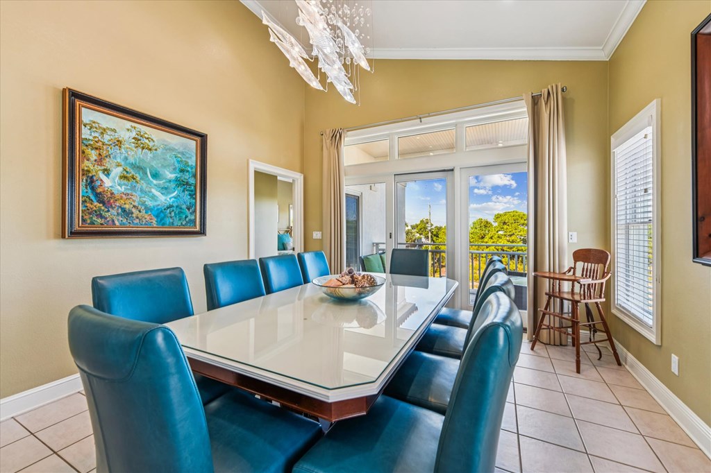 Dining room with teal chairs, a glass-top table, and sliding doors to a balcony.
