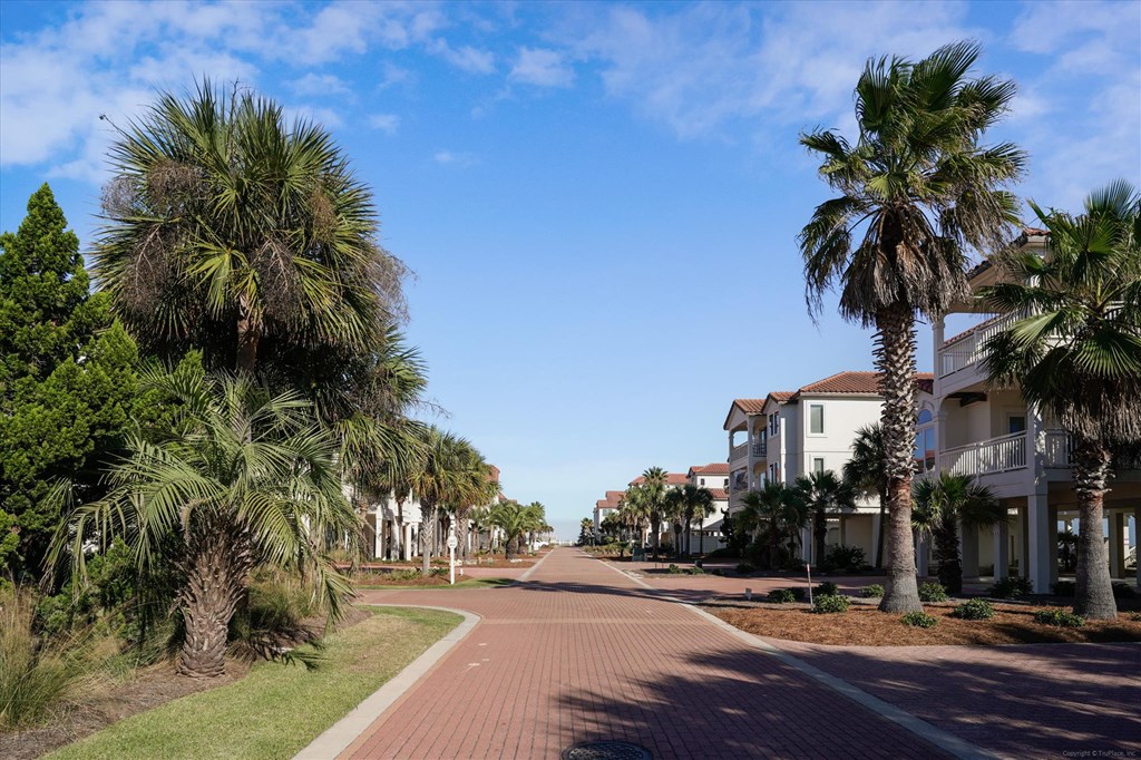 Palm-lined brick street with coastal-style homes and balconies.