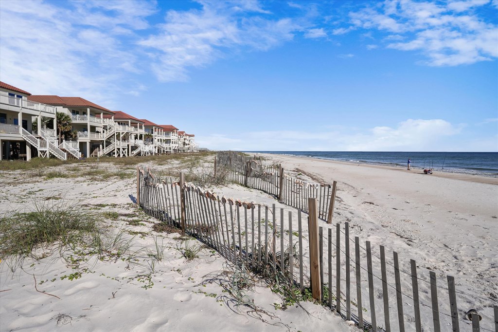 Sandy beach with a weathered dune fence, beachfront houses, and ocean.