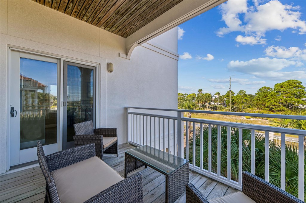 Furnished balcony with wicker seating and a glass-top table overlooking palm trees.