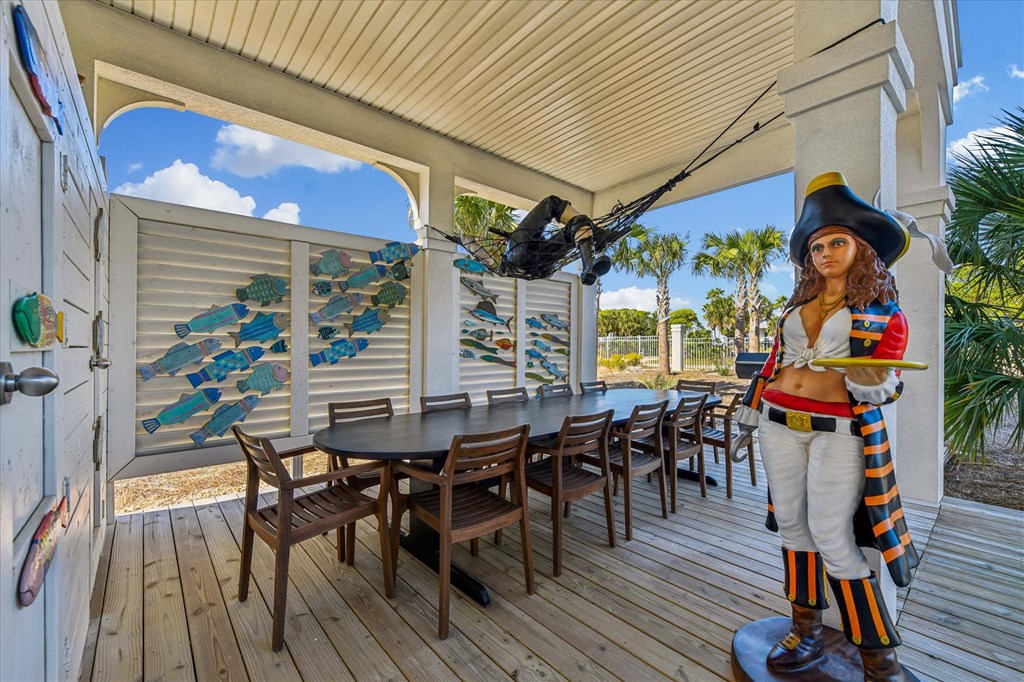 Covered patio with a long dining table, colorful fish wall decorations, and a pirate statue.