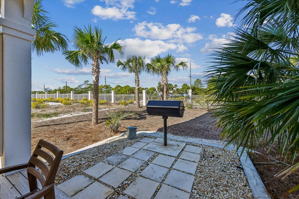 Outdoor patio with a freestanding grill, palm trees, and a fenced yard.