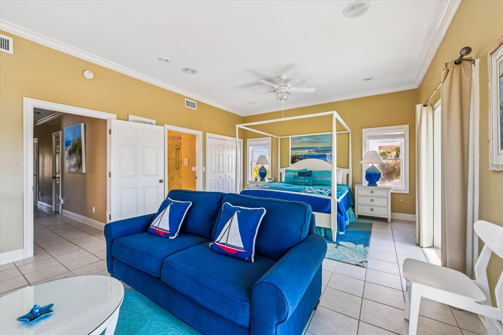 Bedroom with a white canopy bed and bright blue sofa decorated with sailboat pillows.