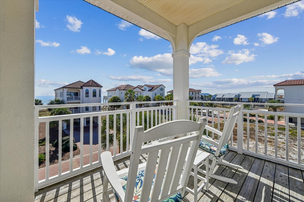 Covered balcony with white rocking chairs overlooking coastal homes and water.