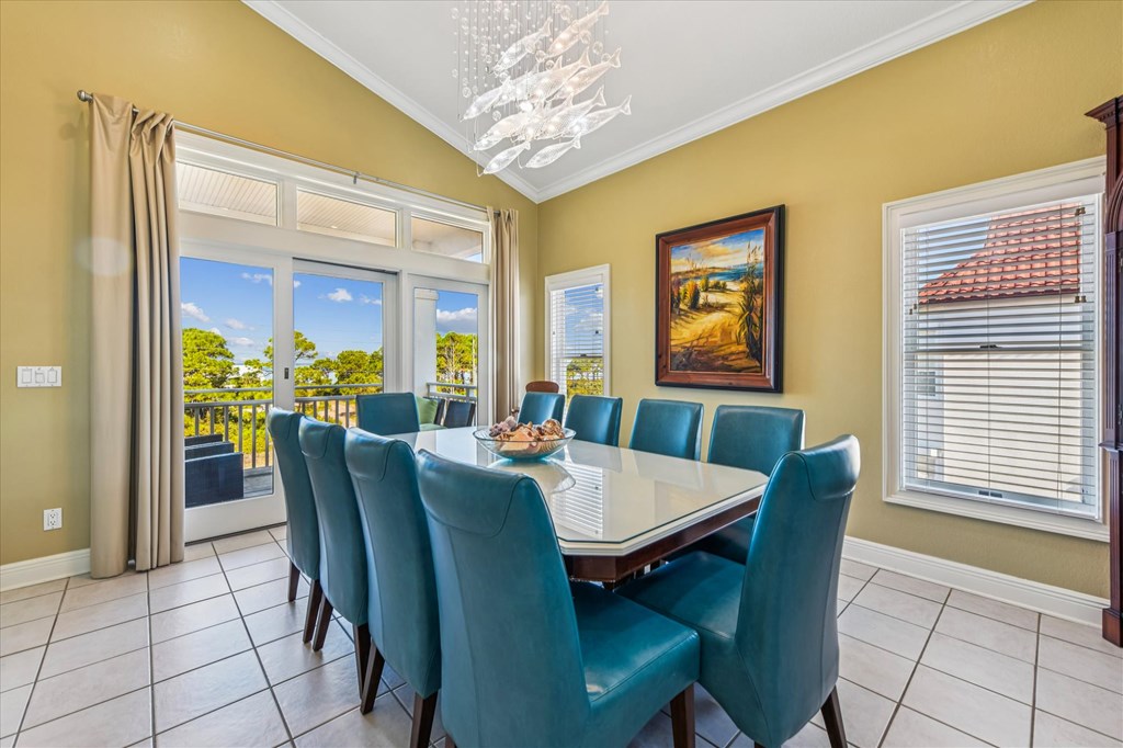 Dining room with a glass-top table, teal chairs, and large windows overlooking trees.
