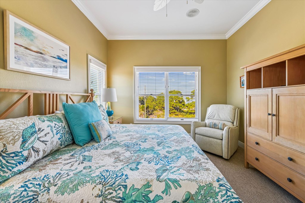Furnished bedroom with a blue-green floral bedspread, wooden wardrobe, and window overlooking trees.