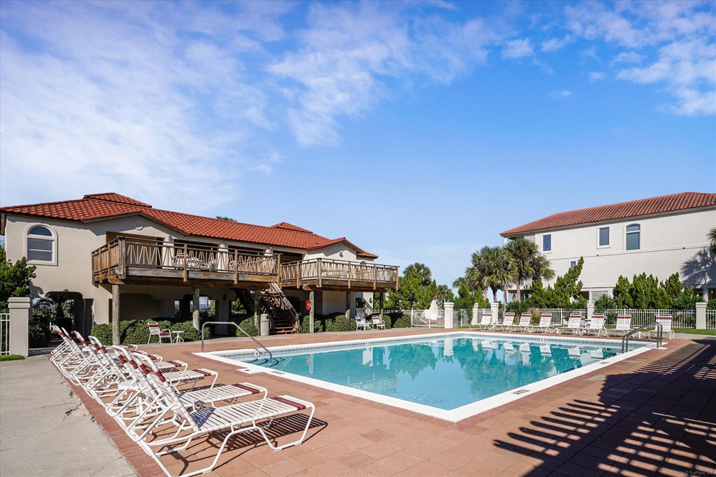 Outdoor swimming pool with rows of lounge chairs and residential buildings around the deck.