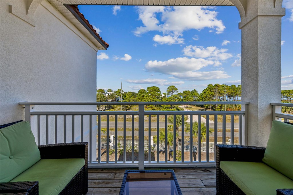 Covered balcony with wicker seating overlooks a tree-lined road under a bright blue sky.