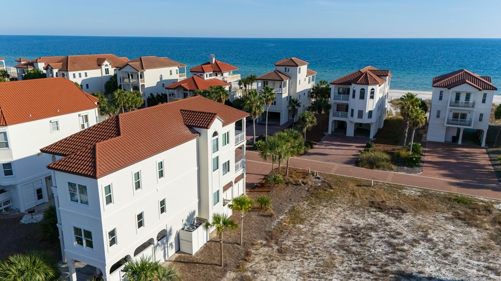 Aerial view of coastal homes with red tile roofs beside the ocean.