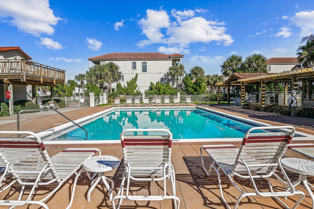 Outdoor pool with turquoise water, white lounge chairs, and a covered pergola.