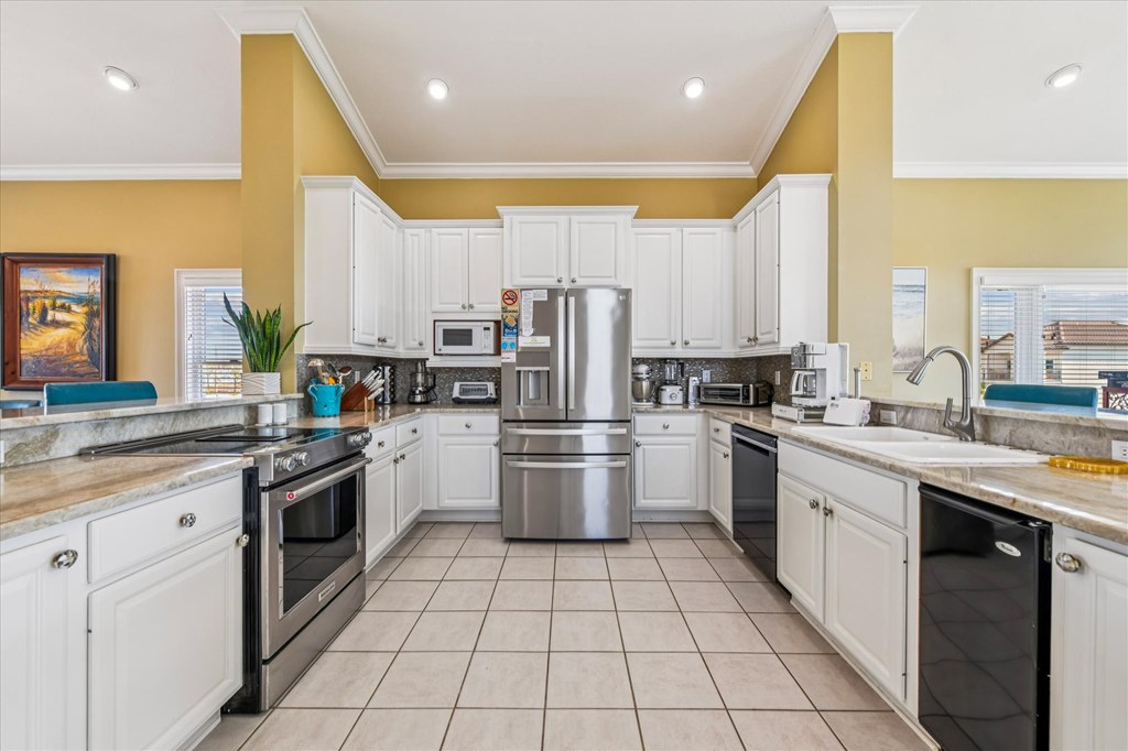 Kitchen with white cabinetry, stainless steel appliances, stone counters, and yellow walls.