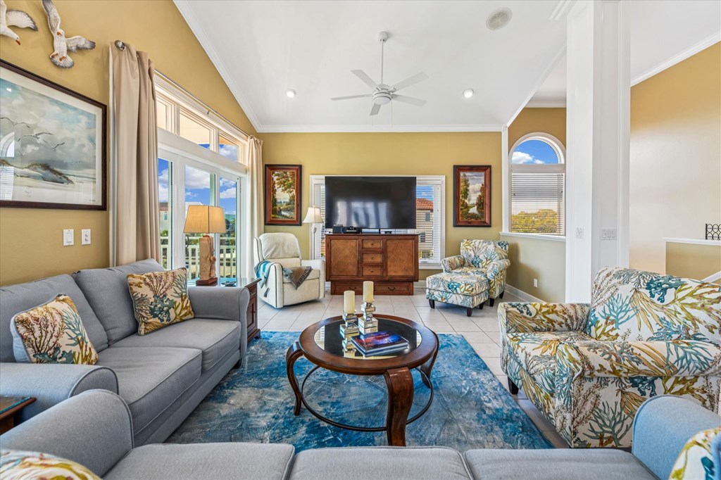 Furnished living room with gray sofas, patterned armchairs, and large windows facing a bright outdoor view.