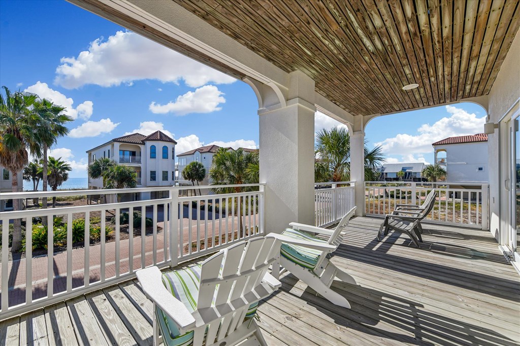 Covered wooden deck with striped lounge chairs and views of nearby homes and water.