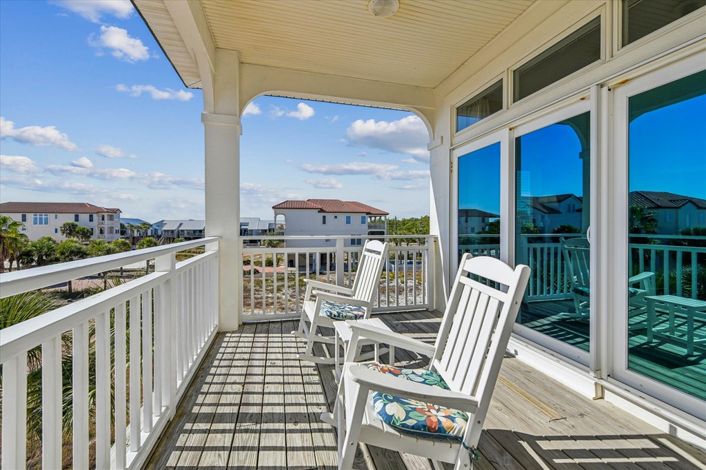 Covered balcony with cushioned rocking chairs overlooking neighboring homes.