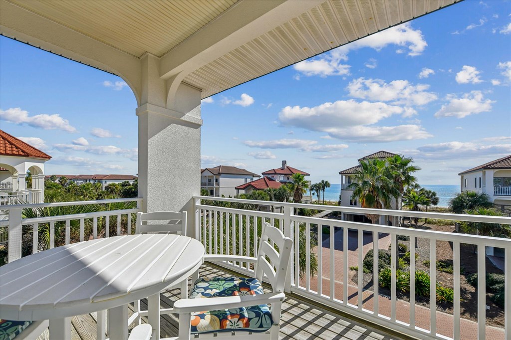 Covered balcony with outdoor dining set overlooking the ocean and neighboring homes.