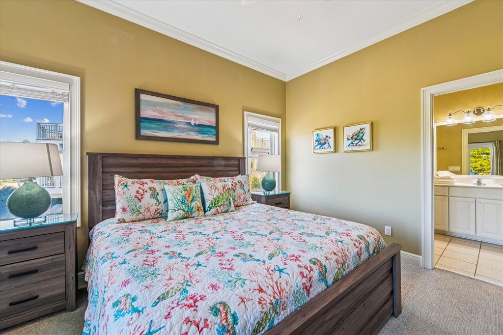 Bedroom with colorful coastal bedding, dark wood furniture, and water visible through the windows.