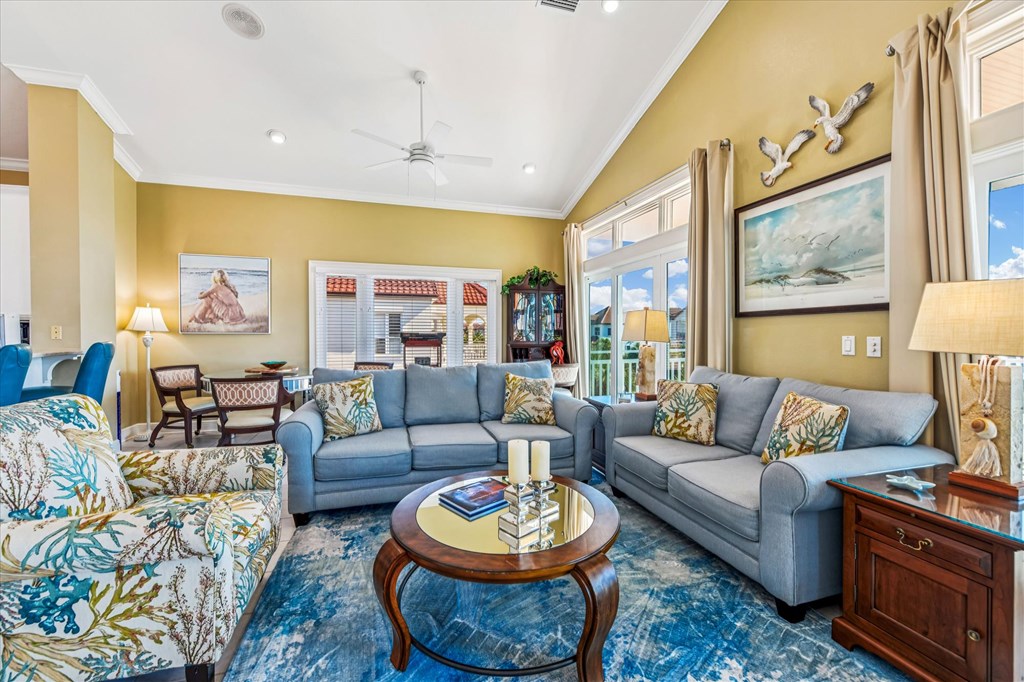 Living room with blue-gray sectional sofas, a patterned armchair, and large windows overlooking neighboring homes.