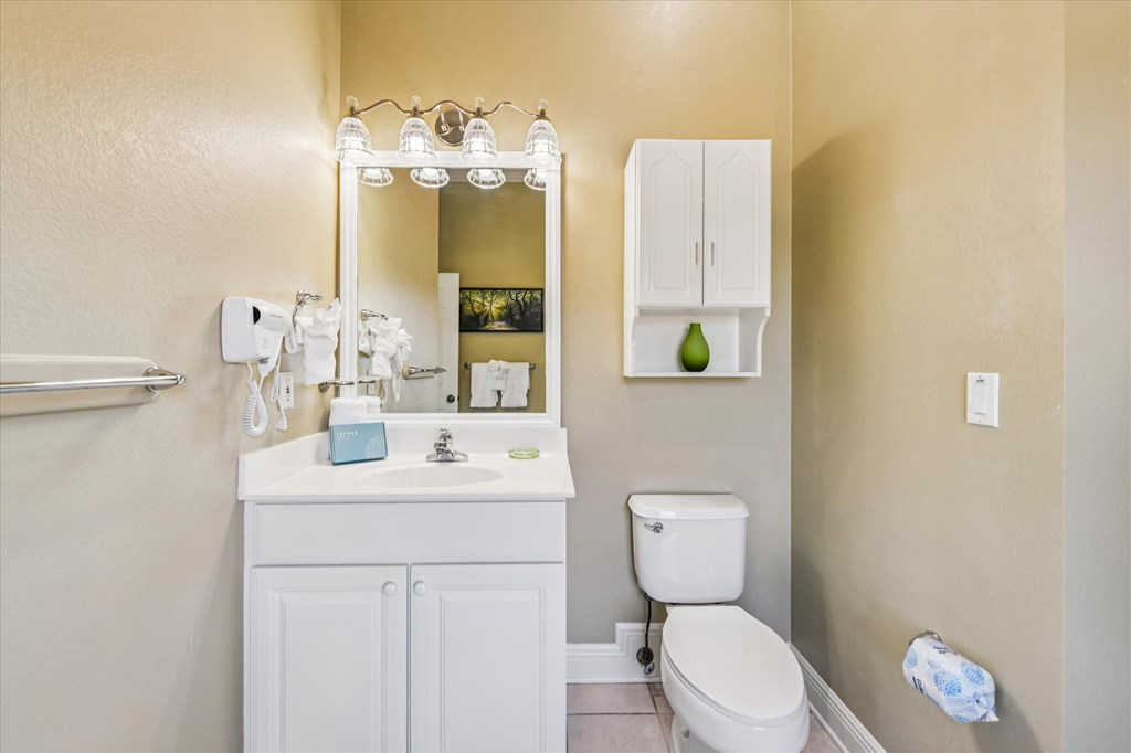 Bathroom with a white vanity, illuminated mirror, toilet, and wall-mounted storage cabinet.