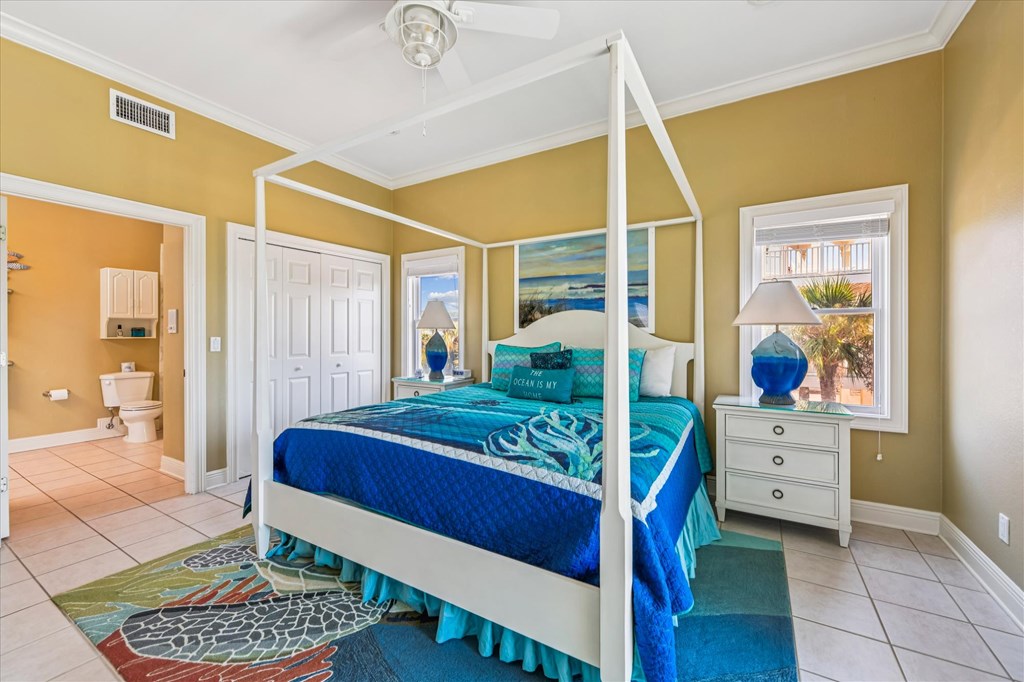 Bedroom with a white four-poster bed, blue ocean-themed bedding, and an adjoining bathroom doorway.